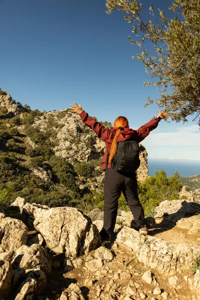 Bir dağın tepesinde kollarını kaldırarak, başarı ve başarı kavramını kutlayan bir kadın yürüyüşçünün dikey görüntüsü