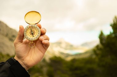 Erkek el dağda bir pusula tutuyor. Arka planda gri bulutlar, doğada yön bulma.