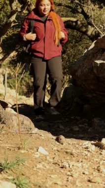 Güneşli bir günde dağ yolunda yürüyen maceraperest bir kadının dikey videosu.