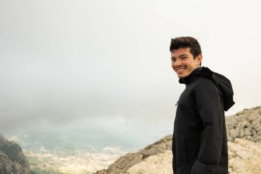 Dağların tepesinde gülümseyen bir yürüyüşçü. Arka planda dağlarla çevrili bir köy. Kopya uzayıyla.