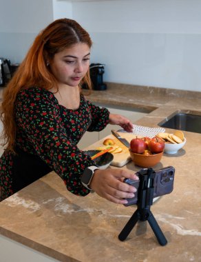 Cep telefonunu ayarlayan genç bir kadının dikey görüntüsü evde bir tatlı tarifini kaydetmeye başlıyor.