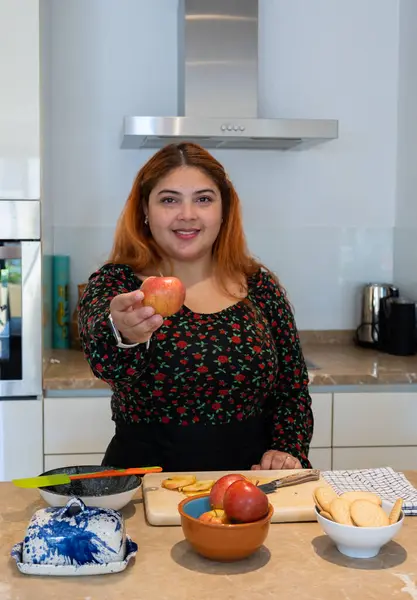 Çilli kızıl saçlı genç kadının dikey görüntüsü. Evde tatlı tarifi hazırlayan elmayı gösteriyor.