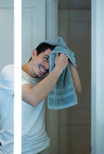 Duş aldıktan sonra saçlarını parlak bir aynanın önünde havluyla kurutan neşeli adamın dikey görüntüsü.