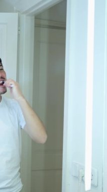 Adamın dikey videosu uyandı, banyo aynasının önünde dişlerini fırçalıyor, kişisel hijyen...