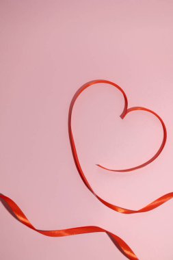 İzole edilmiş pembe bir zemin üzerinde sevgililer günü kalbi şeklinde kırmızı kurdelenin dikey görüntüsü, sevgi ve şefkat kavramı.