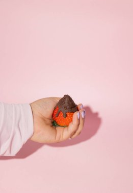 Vertical image of female hand holding a strawberry with melted chocolate on a pink background, Valentine's Day food concept clipart