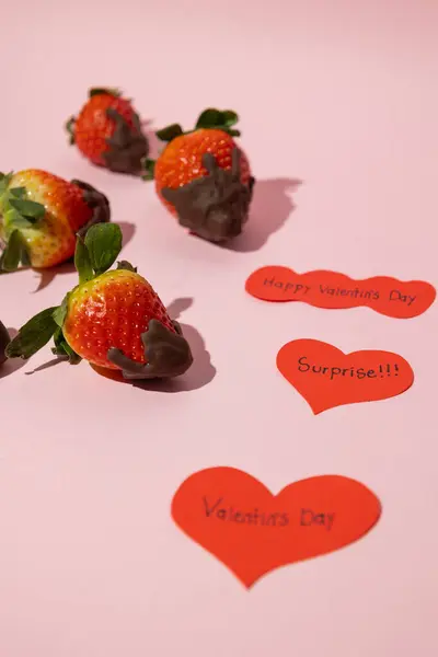 Kalplerin dikey görüntüsünü Sevgililer Günü cümleleri ve erimiş çikolatalı çileklerin pembe arka planda, Sevgililer Günü yemek konseptiyle kapat