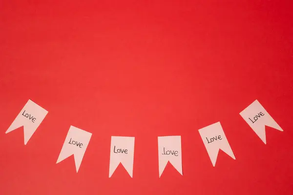 Üzerinde aşk cümlesi yazılı pembe kağıt flamalar kırmızı arka planda fotokopi alanı ile gruplandırılmış. Sevgililer Günü
