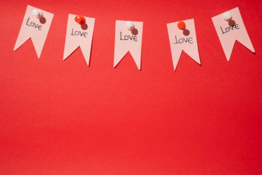 Pink paper pennants with love phrase written on them grouped together stuck with thumbtacks on a red background with copy space. Valentine's Day clipart