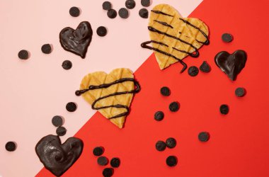 Heart shaped cookies with melted chocolate and chocolate hearts with sprinkles scattered on a pink and red background. Valentine's Day concept clipart