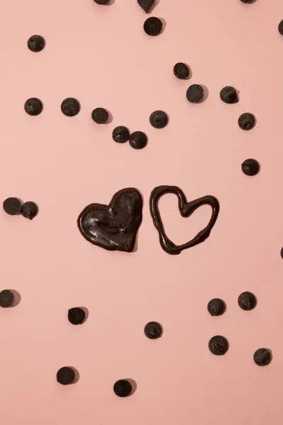 Çikolata dolu kalbin dikey görüntüsü ve pembe arka planda serpiştirilmiş çikolata parçacıkları ile doldurulmamış kalp. Sevgililer Günü konsepti