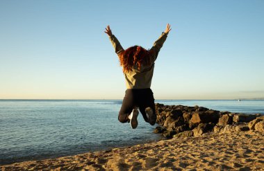 Genç bir kadın bir kış sabahı sahilde neşeyle zıplıyor. Yaşam biçimi