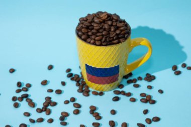 Top view of glass with Colombian flag filled with coffee beans on a light blue background, Colombian culture and coffee concept clipart