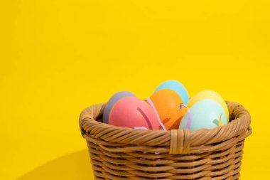 Çoklu renkli paskalya yumurtalarını fotokopi alanı olan sarı bir arka planda saman sepetine koy. Paskalya Sanatları konsepti