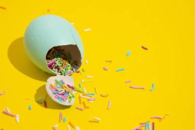 Açık mavi yumurta kabuğunu kapat. Sarı arka planda renkli şekerler dağıt. Paskalya tatlıları ve dekorasyon konsepti