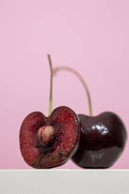 Beyaz ahşap bir rafta ikiye bölünmüş küçük yuvarlak kırmızı meyveli ve ortasında tohum olan kiraz ağacının dikey görüntüsü.