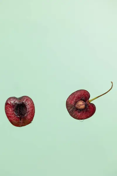 Kirazın dikey görüntüsü ikiye bölünmüş açık yeşil zemin üzerine düşmüş, ortasında tohum olan küçük yuvarlak kırmızı meyve