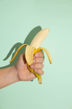 Açık yeşil zemin üzerinde muz tutan bir erkeğin dikey görüntüsü. Potasyum açısından zengin sarı tropik meyve.