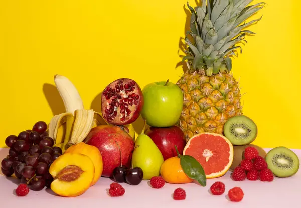 Sarı arka planda pembe, ananas, muz, kivi, üzüm, şeftali, armut, elma, ahududu, kiraz, nar, mandalina, greyfurt içeren renkli tropikal meyveler. sağlıklı yiyecekler