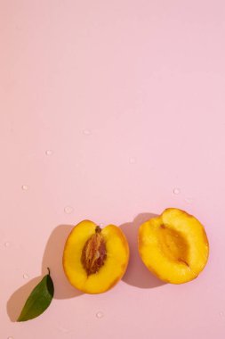 Pembe arkaplandaki yarım şeftalinin dikey üst görünümü ve kopyalama alanı. Kadife tenli portakal meyvesi ve sulu, tatlı ve aromatik posa.