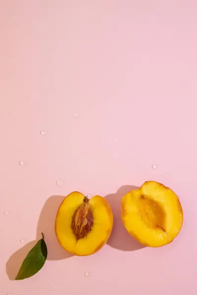 Pembe arkaplandaki yarım şeftalinin dikey üst görünümü ve kopyalama alanı. Kadife tenli portakal meyvesi ve sulu, tatlı ve aromatik posa.