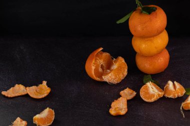 Fresh mandarins stacked on a rustic background with peeled mandarins scattered around. Dark food clipart