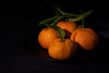Siyah bir plaka üzerinde siyah bir arka planda fotokopi alanı olan Mandarinler. C vitamini açısından zengin sağlıklı meyve.