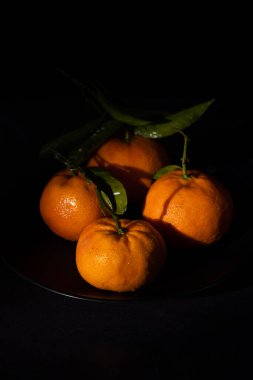 Siyah bir plaka üzerinde fotokopi uzayı olan mandalinaların dikey görüntüsü. C vitamini açısından zengin sağlıklı meyve.