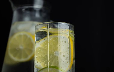 Koyu arkaplanda limon dilimleri olan bir sürahinin yanında limonata ile cam camı kapat. Narenciye içeceği tazeleniyor
