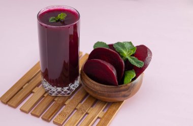 Hafif arka planda pancar dilimleri olan ahşap bir kasenin yanında pancar püresi yüksek antioksidanlı koyu kırmızı bir içecek.