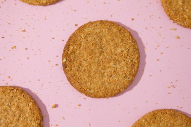 Tam tahıllı yulaf ezmesi kurabiyeleri pastel pembe zemin üzerine yayılmış, buğday unuyla yulaf gevreğiyle karıştırılmış kurabiyeler, geleneksel pişirme.