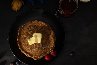 Üzerine erimiş tereyağı sürülmüş tam buğday unundan yapılmış krep ve yanında siyah bir tabakta ahududu. Ev yapımı yemekler, karanlık yemekler.