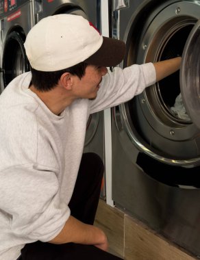 Genç adam çamaşırhanedeki çamaşır makinesine elbiselerini koyuyor. Yaşam biçimi