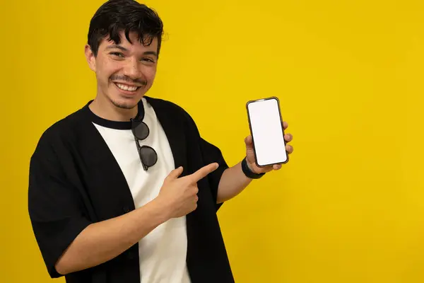 Çilli bıyıklı genç adam elini cep telefonunun boş ekranına doğrulturken gülümsüyor. Sarı arka planda reklam için yer var.