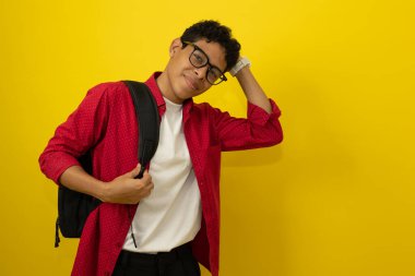 Genç, kahverengi tenli, Latin bir adam. Kolej öğrencisi, günlük kırmızı kıyafetler giyiyor. Sarı arka planda sakince gülümsüyor.