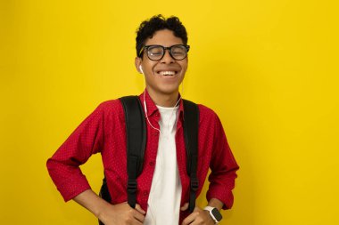 Genç, kahverengi tenli Latin bir adam, gündelik kırmızı kıyafetler giyen üniversite öğrencisi mutlu bir şekilde gülümsüyor sarı arka planda kopya alanı ile gözleri kapalı.