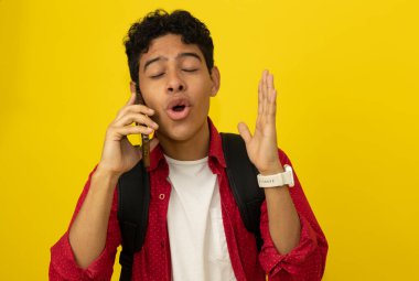 Kırmızı üniformalı, siyah çantalı, kahverengi tenli genç bir öğrenci sarı arka planda, fotokopi alanı olan bir cep telefonuyla konuşuyor.