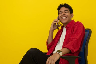 Ofis sandalyesinde oturan neşeli, genç bir Latin 'in cep telefonuyla fotokopi çeken sarı bir arka planda konuşmasının yakın plan fotoğrafı.