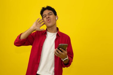 Genç Latin adam kablosuz kulaklıklarla müzik dinliyor sarı arka planda reklam için yer var.
