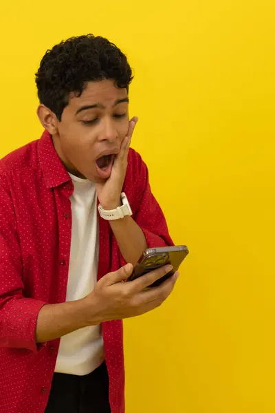 Yüzünde eli olan kahverengi tenli genç bir adamın dikey görüntüsü, şaşırmış, sarı arka plandaki cep telefonuna bakarken reklam yazmak için yeri vardı.