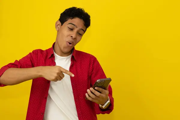 Heyecanlı genç Latin bir adam cep telefonunu işaret ederek sarı bir arka planda reklam yazmak için boşluk yaratıyor.