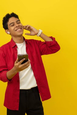 Dinlediği müzikten hoşlanan genç bir Latin 'in dikey görüntüsü kablosuz kulaklıkla sarı bir arka planda reklam alanı ile birlikte.