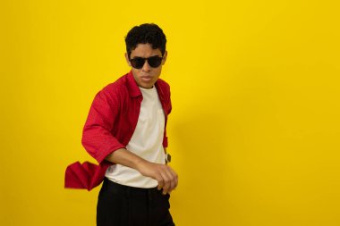 Neşeli, kahverengi tenli, sıradan kırmızı elbiseler giyen, sarı arka planda siyah gözlüklü, fotokopi çeken Latin bir adam.