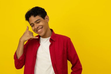 Koyu tenli, neşeli, latin bir adam. Günlük kırmızı giysiler giyiyor. Sarı arka planda, fotokopi çekilen bir el hareketi yapıyor.