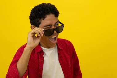 Kırmızı gündelik elbiseli neşeli Latin bir adamın göz kırparken gözlüğünü çıkarması.