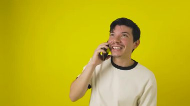 Bıyıklı, siyah gözlüklü, akıllı telefonuyla konuşan genç çilli bir adam. Taklit uzay ile sarı bir arka planda saatine bakarken mutlu bir şekilde konuşuyor.