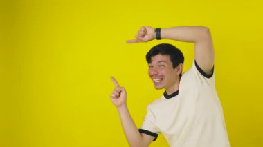 Beyaz tişörtlü, gülümseyen, çilli genç bir adam, sarı arkaplanda yazı için enerji dolu bir yeri işaret ediyor. Reklam için kopyalama alanı olan grafik bir kaynak.