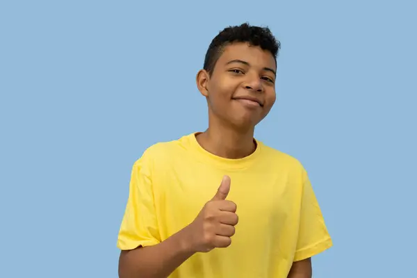 Neşeli koyu tenli Latin ergen, sarı tişörtlü, açık mavi arka planda, kopyalama alanı olan bir jest yapıyor.