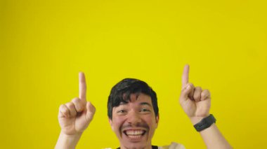 Neşeli, çilli, çok enerjili genç bir adam işaret parmaklarıyla sarı bir arka planda, promosyon alanı kavramının üstündeki boşluğu işaret ediyor.