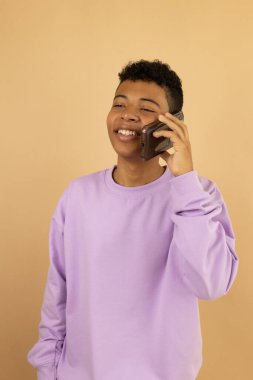 Eflatun eşofman üstü giyen Latin bir gencin profil görüntüsü cep telefonuyla açık kahverengi arka planda mutlu bir şekilde konuşması, akıllı telefondan konuşan genç bir adam konsepti.